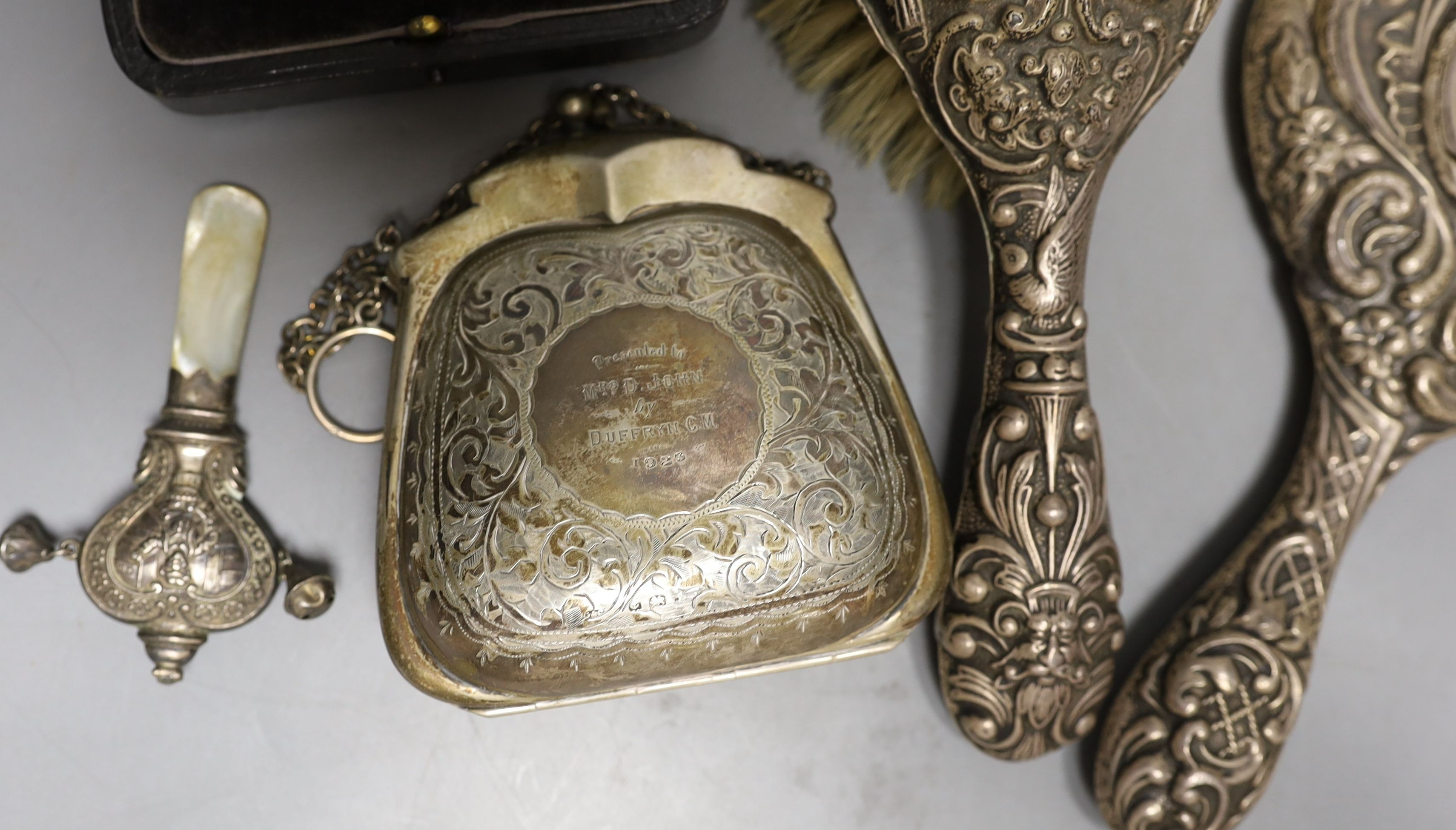 A cased pair of George V silver condiments, an engraved silver purse, silver mounted mirror and brush an a child's silver rattle.